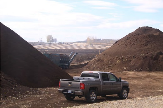 Two large piles of manure. There is a pickup truck in front of the manure piles. The manure piles look about three times taller than the truck.