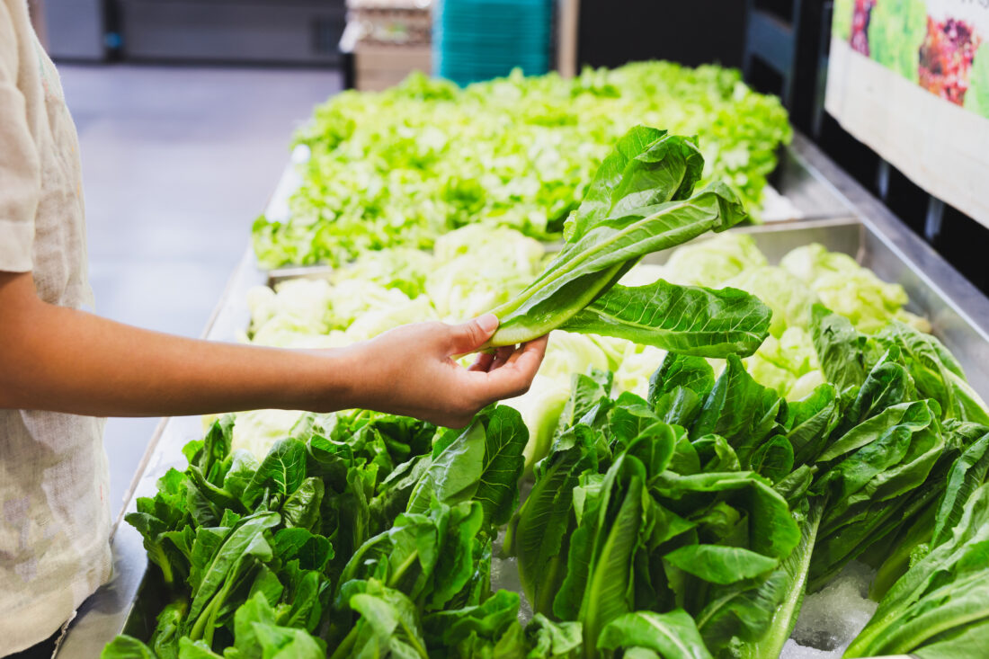 A person's arm picks up a head of lettuce from a bin of lettuces in a grocery store