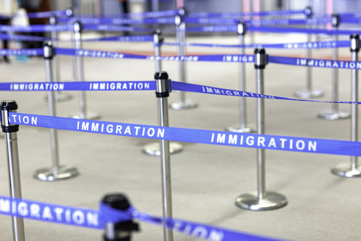 A series of bollards with blue rope reading "IMMIGRATION"