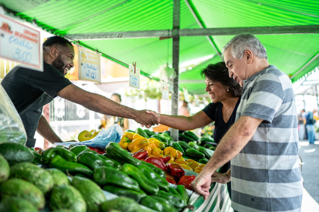 A farmer shakes hand with a customer over crates of vegetables at a farmers' market