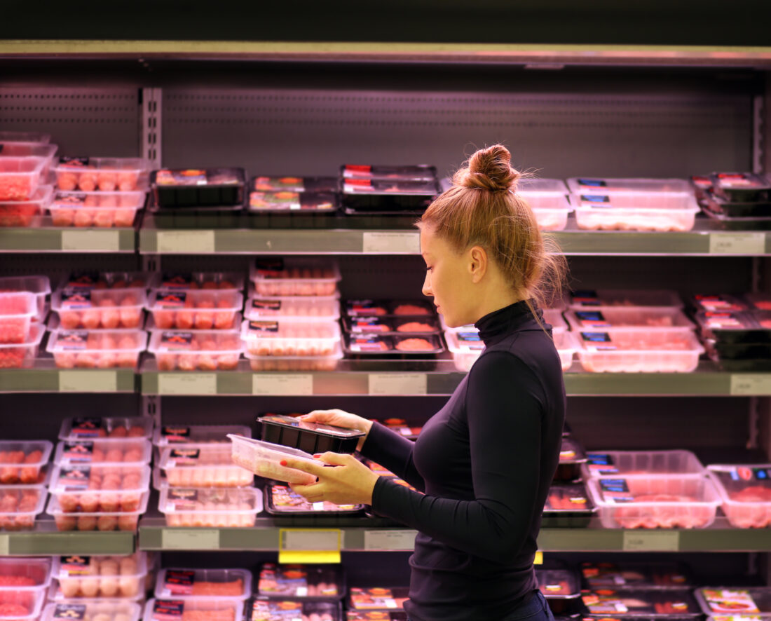 A woman looks at meat products in a case in a supermarket